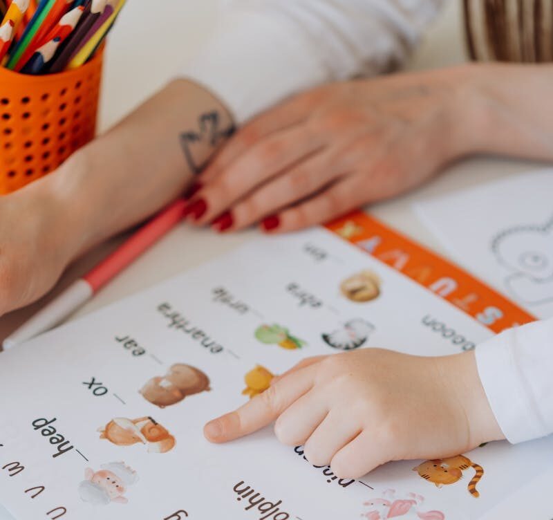 Photo by Mikhail Nilov A child points to animals in a colorful alphabet book, learning letters.